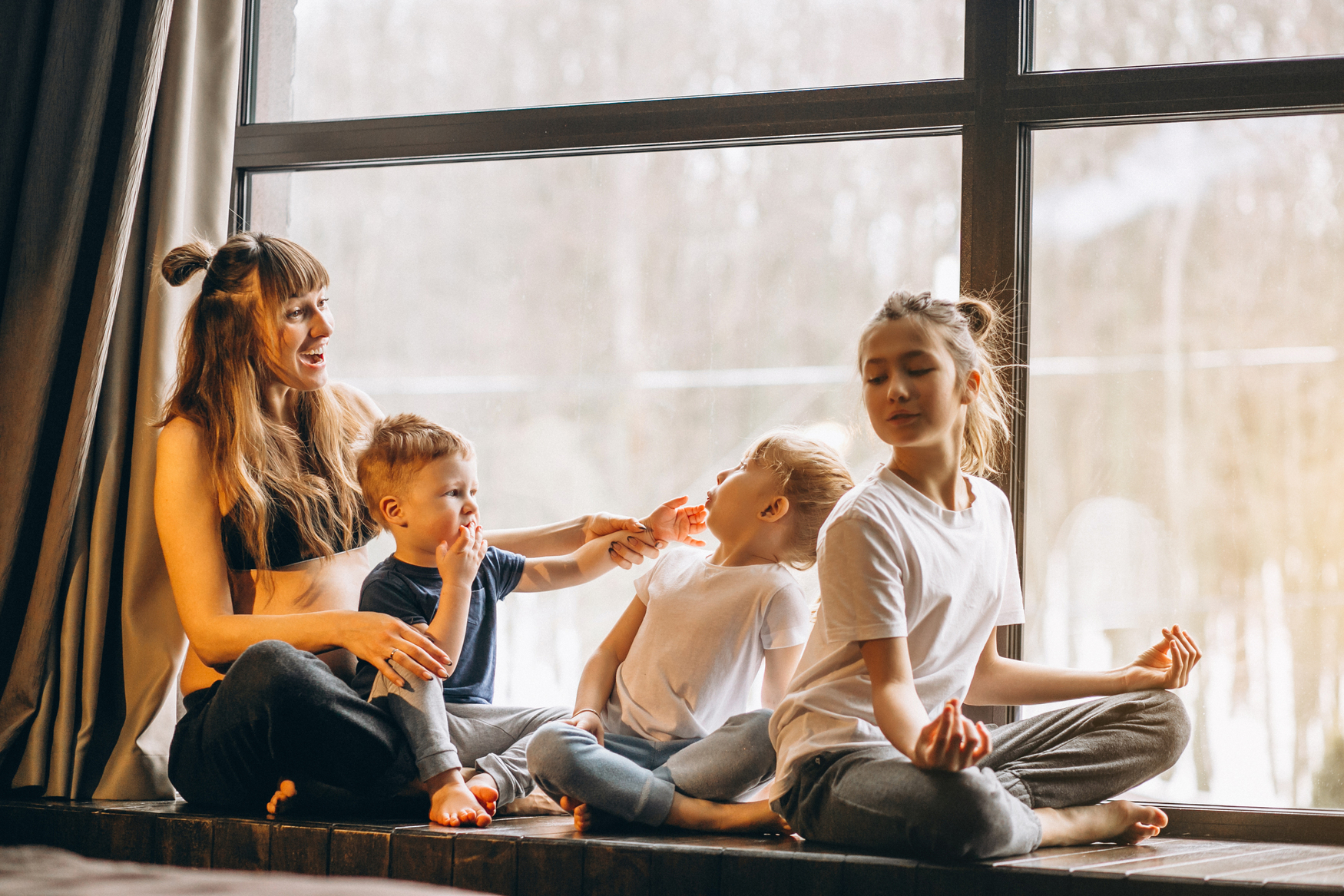 Mindfulness en familia: una mujer con sus tres hijos en una ventana haciendo meditación